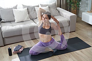 Young girl doing yoga stretching exercise sitting on mat near couch in modern living room