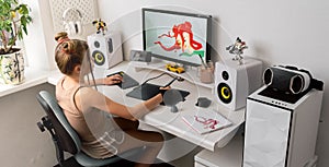 A young girl draws on a PC using a graphics tablet in her comfortable home office.