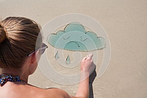 Young girl draws on the sand on the beach a cloud. Weather forecast, mood. Cloudy, overcast