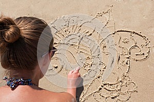 Young girl draws on the sand on the beach a zentangle, doodle.