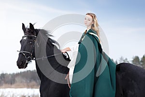 Young girl in dress with black horse in winter