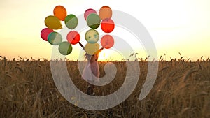 Young girl in the dress with colorful ballons is running across the field.