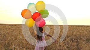 Young girl in the dress with colorful ballons is running across the field.