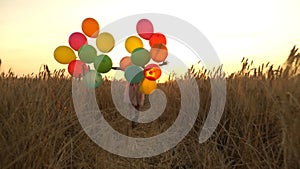 Young girl in the dress with colorful ballons is running across the field.