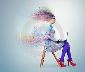 Young girl in dress and glasses sitting on a chair with laptop