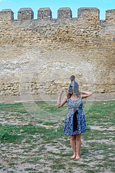 Young girl in a dress with a helmet on her head near the fortress wall