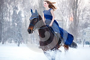 Young girl in dress riding horse on winter field