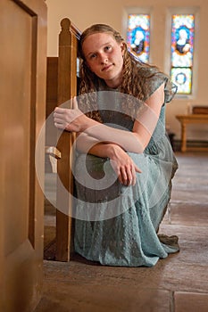 Young girl in a dress sitting in a prayerful gesture on the floor of a church