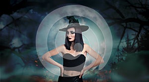 Young girl dressed as witch in misty forest on full moon night. Halloween fantasy