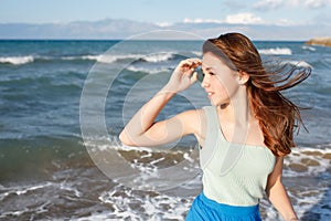 A young girl dressed in bright clothes in the color of the sea looks to the side, her hair flutters in the wind, the background of