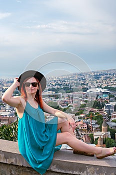 A young girl dressed in a bright dress and hat poses against the backdrop of a view of the city. The concept of recreation and