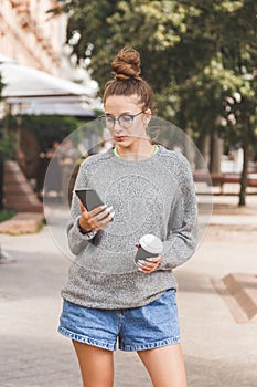 Young girl dressed in casual clothes with phone and a cup of takeaway coffee. Daily life of youth. People online