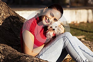 Young girl dressed in red together with her little dog  poured in red  toothed on the trunk of a tree in a natural park