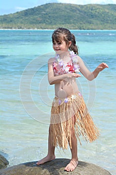 Young girl dressed up as a hula girl dance against blue lagoon a