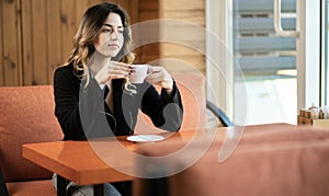 young girl drinking hot coffee or tea enjoying it while sitting in cafe. happy teen holding a cup of coffee.