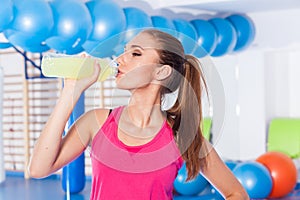 Young girl drinking isotonic drink, gym.