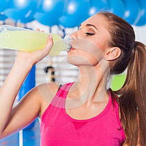 Young girl drinking isotonic drink, gym