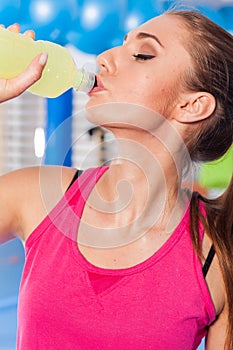 Young girl drinking isotonic drink, gym