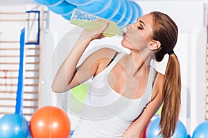 Young girl drinking isotonic drink, gym. She is happy