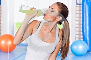 Young girl drinking isotonic drink, gym. She is happy