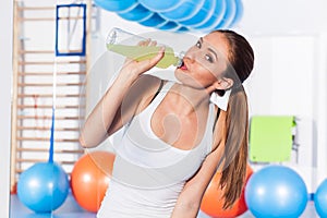 Young girl drinking isotonic drink, gym. She is happy and full of emotion.