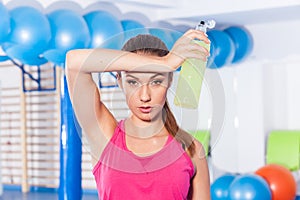 Young girl drinking isotonic drink, gym. She is wiping sweat
