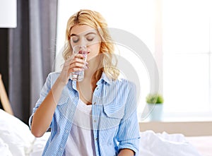 Young   girl drinking water glass in bed in the morning