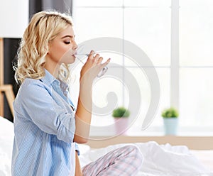 Young   girl drinking water glass in bed in the morning
