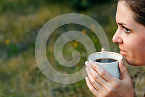 A young girl drinks coffee and looks into the distance to the sunset, waiting for someone. The concept of expectation, longing,