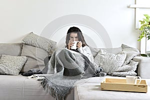 The young girl drinks tea on a gray sofa