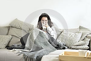 The young girl drinks tea on a gray sofa