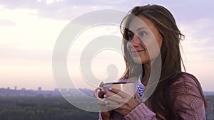 A young girl drinks a warm drink and enjoys the sunset