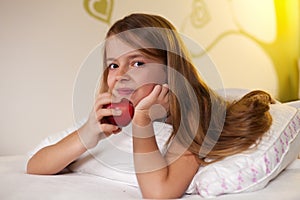 Young girl eating an apple in bed