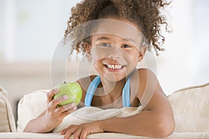 Young girl eating apple in living room smiling