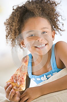 Young girl eating pizza slice in living room