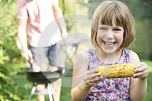 Young Girl Eating Sweetcorn At Family Barbeque photo