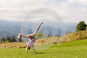 Young girl energetic child doing a cartwheel outdoors, outside on the grass, mountains in the background Freedom, vitality,