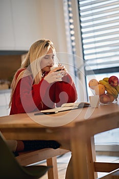A young girl enjoying a coffee while studying at the kitchen. Routine, student, morning