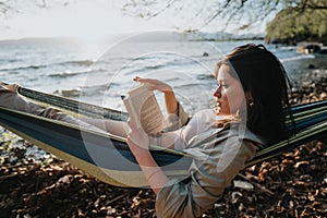 Young girl enjoying a lovely book in a hammock by the lake at sunset