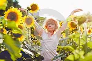Young girl enjoying nature on the field of sunflowers at sunset, portrait of the beautiful redheaded woman girl with a sunflowers