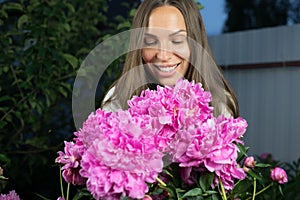 Young girl in evening garden enjoys bouquet of pink peonies.