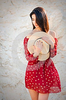 A young girl in expectation on a sandy background in a red light dress and hat