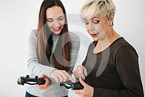 A young girl explains to an elderly woman how to use the joystick for video games. Joint pastime. Modern technologies