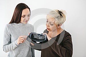 A young girl explains to an elderly woman how to use virtual reality glasses. The older generation and new technologies.