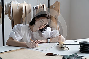 Young girl fashion designer write notes of measurements planning new collection in sewing studio