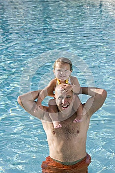 Young girl on father shoulders in swimming pool