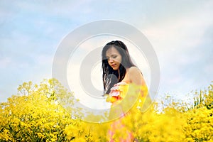 Young girl on the field with yellow flowers Sun rays and blue sky