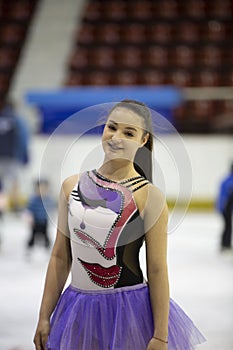 Young girl a figure skater in purple dress on an ice arena