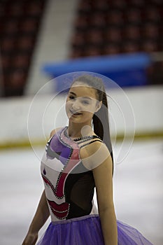 Young girl a figure skater in purple dress on an ice arena