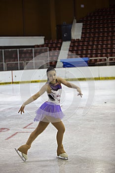 Young girl a figure skater in purple dress on an ice arena